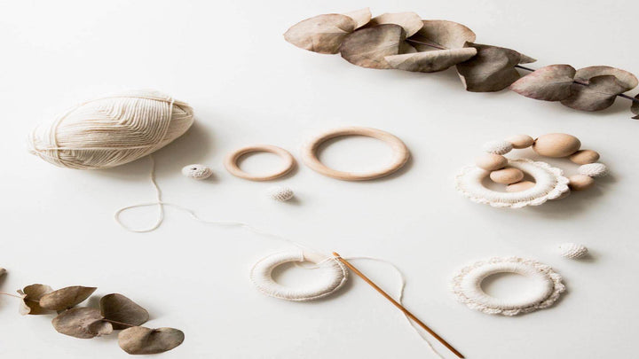 Photo of dried leaves, wooden hoops, beads and white yarn on a white background, for e1011 Labs' page on hemp jewelry and making hemp bracelets.